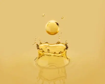 Image of a golden drop of a seed oil dripping and bouncing back into the air.