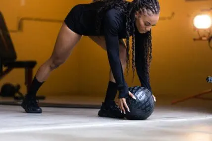 image of a woman grabbing a medicine ball for her workout routine