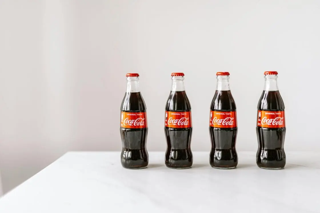 Image of four small glass bottles of Coca-Cola on a white table against a white backdrop.