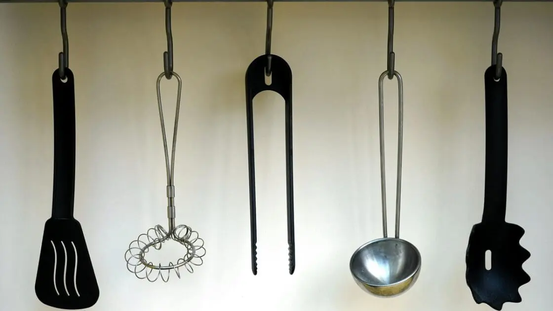Image of a black plastic spatula and other plastic utensils hanging on hooks in a kitchen.