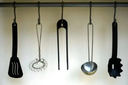 Image of a black plastic spatula and other plastic utensils hanging on hooks in a kitchen.