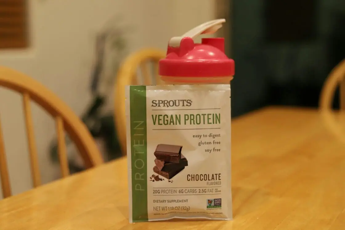 Image of a packet of plant-based protein in a pouch leaning on a reusable protein shake bottle.
