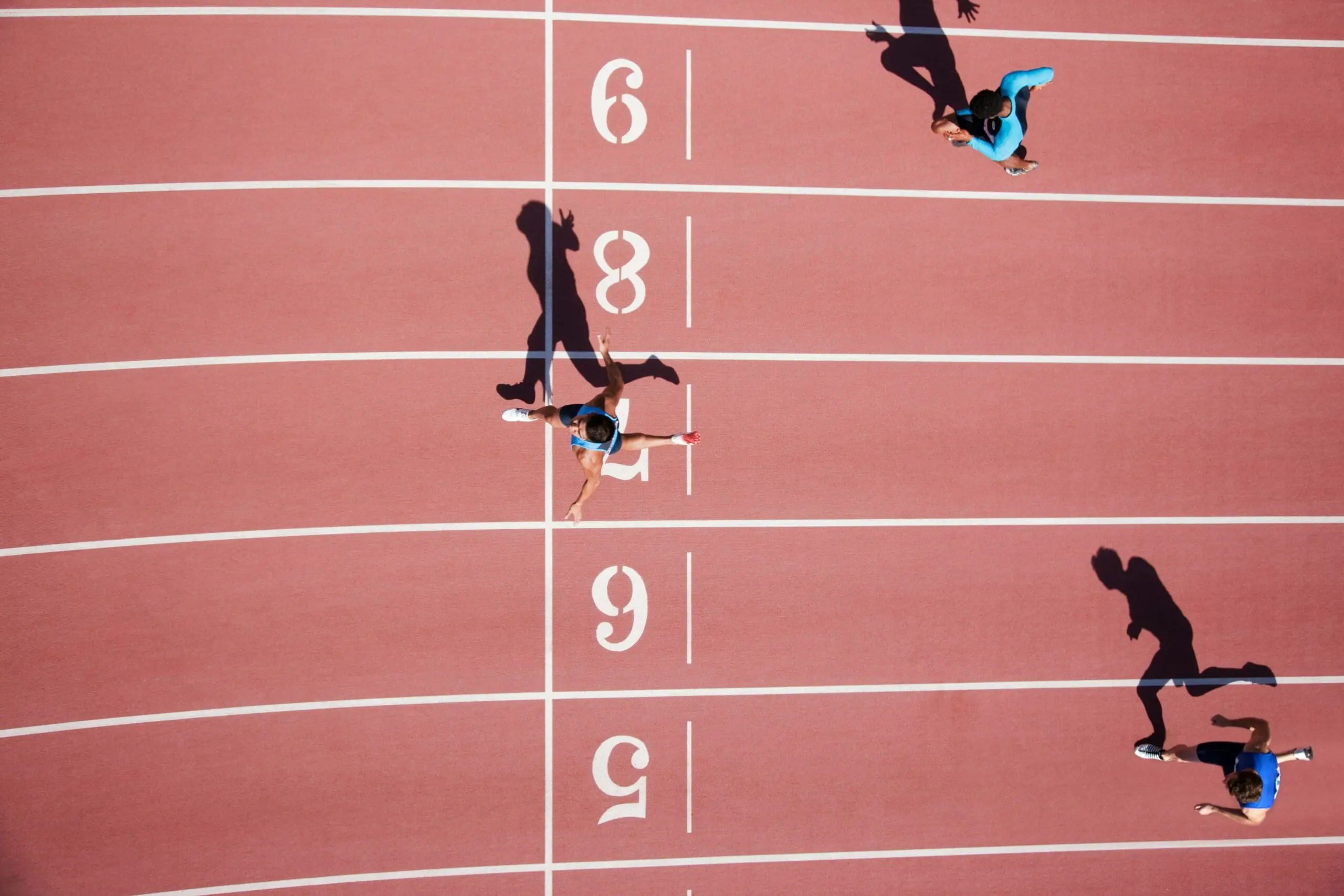 Image of three racers crossing the finish line in a sprint on a track from an overhead view.