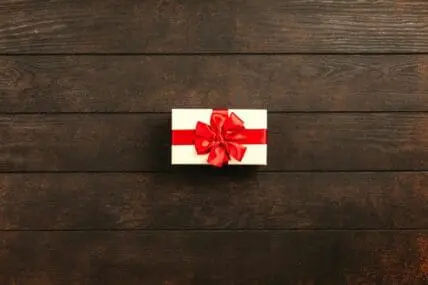 Image of a small white gift box with a red ribbon on a wooden tabletop.