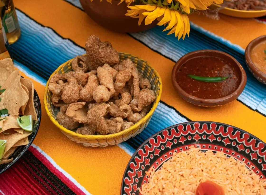 Image of a colorful bowl full of pork rinds on a table with a brightly colored tablecloth.