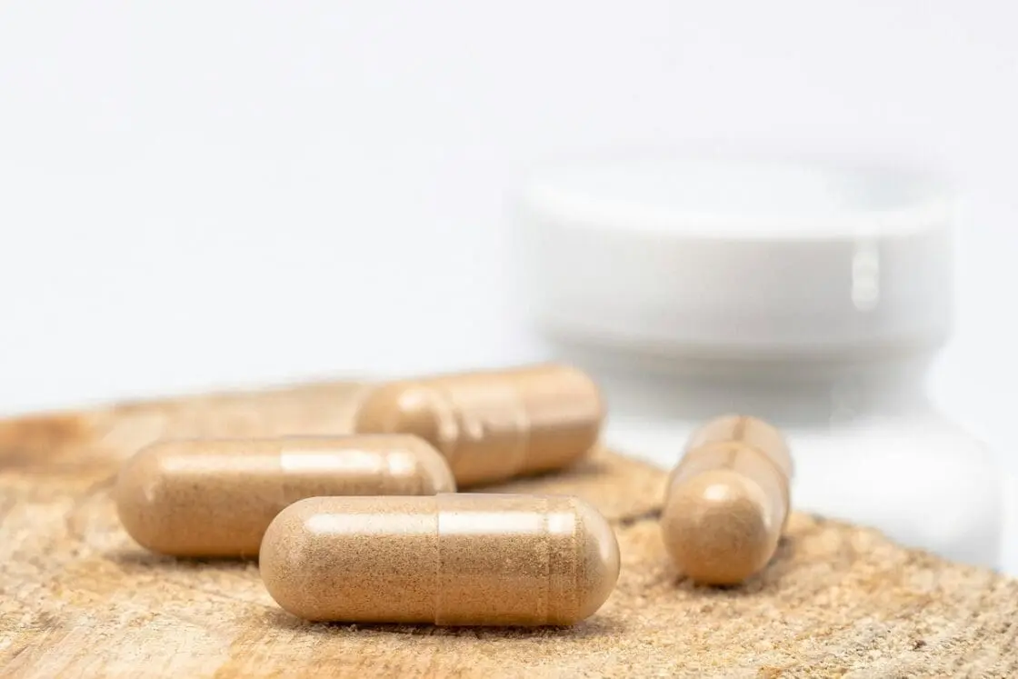Image of several supplement capsules filled with collagen powder on a wooden tabletop with a pill bottle in the background.