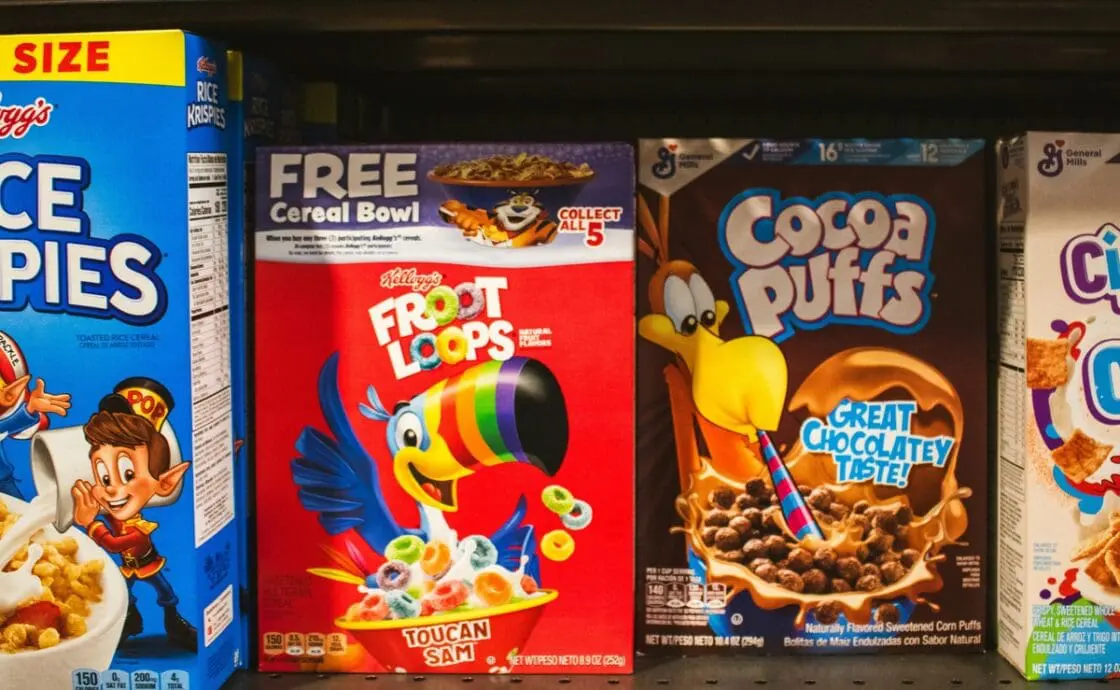 Image of several boxes of cereal lined up in a grocery store aisle, including Froot Loops and Cocoa Puffs.