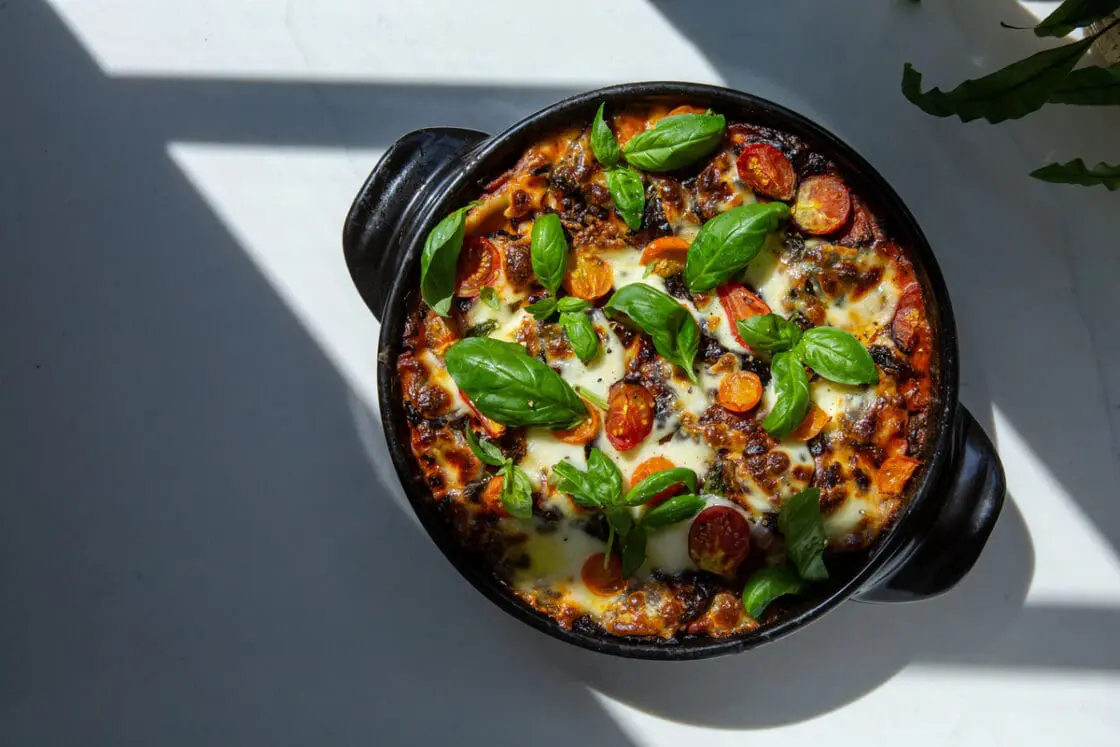 Image of the ceramic 10-quart Dutch Oven from Xtrema Cookware, with a baked pasta dish covered in melted cheese and fresh basil.