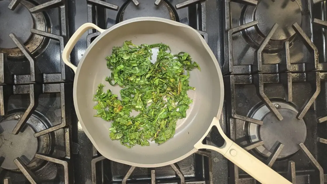 Image of the Our Place Always Pan 2.0 on a black stovetop, filled with bright fried greens.