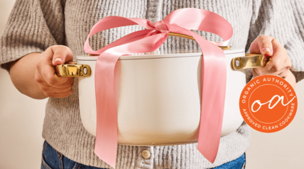 Image of a woman holding a Caraway stockpot in cream, with a large pink ribbon on top to present it as a gift.