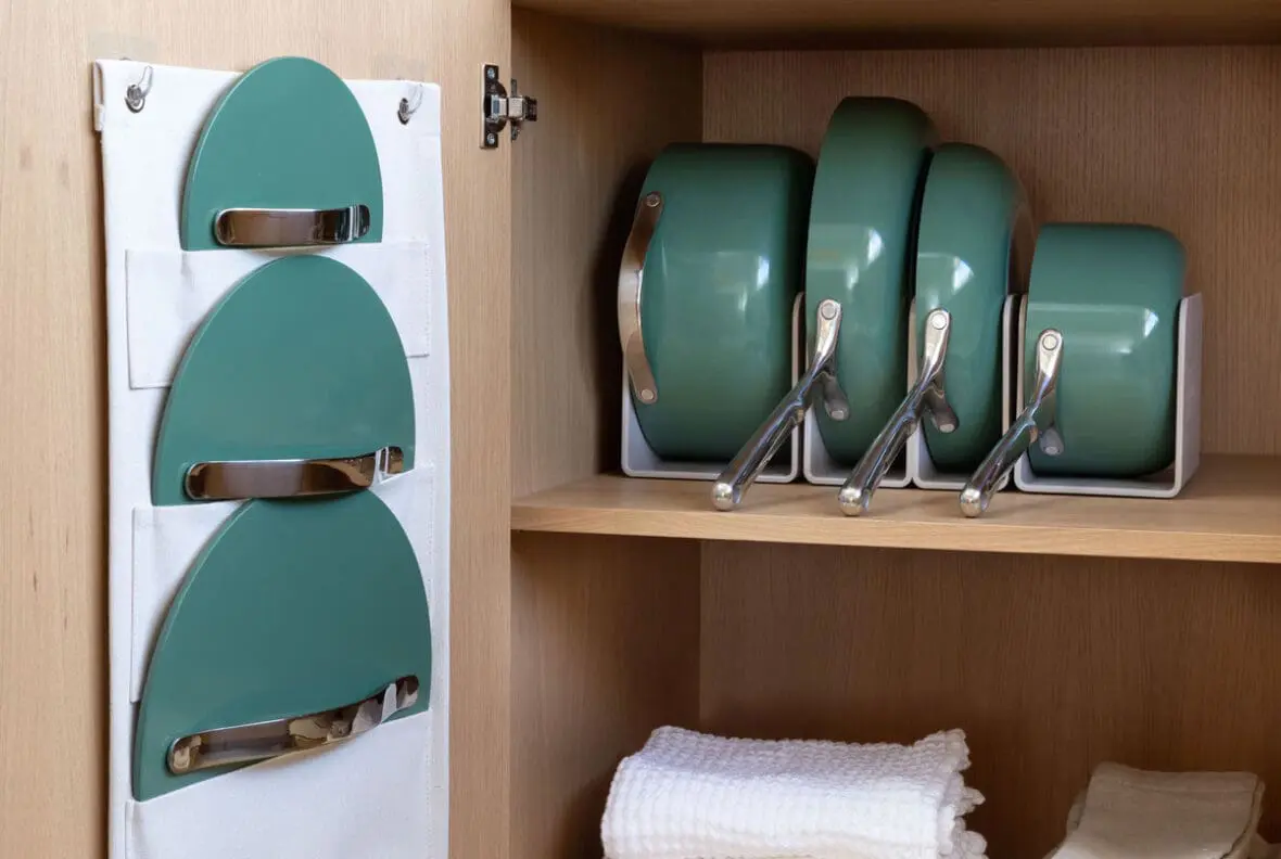 Image of the Caraway Cookware set in sage, shown tucked away in a cupboard on the magnetic pan racks and canvas lid holders.