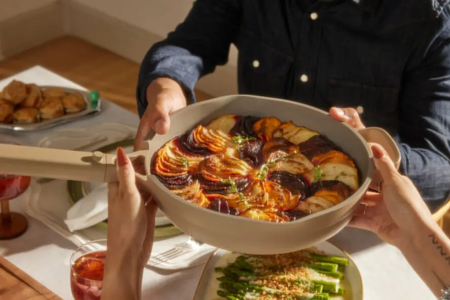 Image of the Our Place Always Pan being used as a holiday serving dish, held by a pair of hands over a dining table.