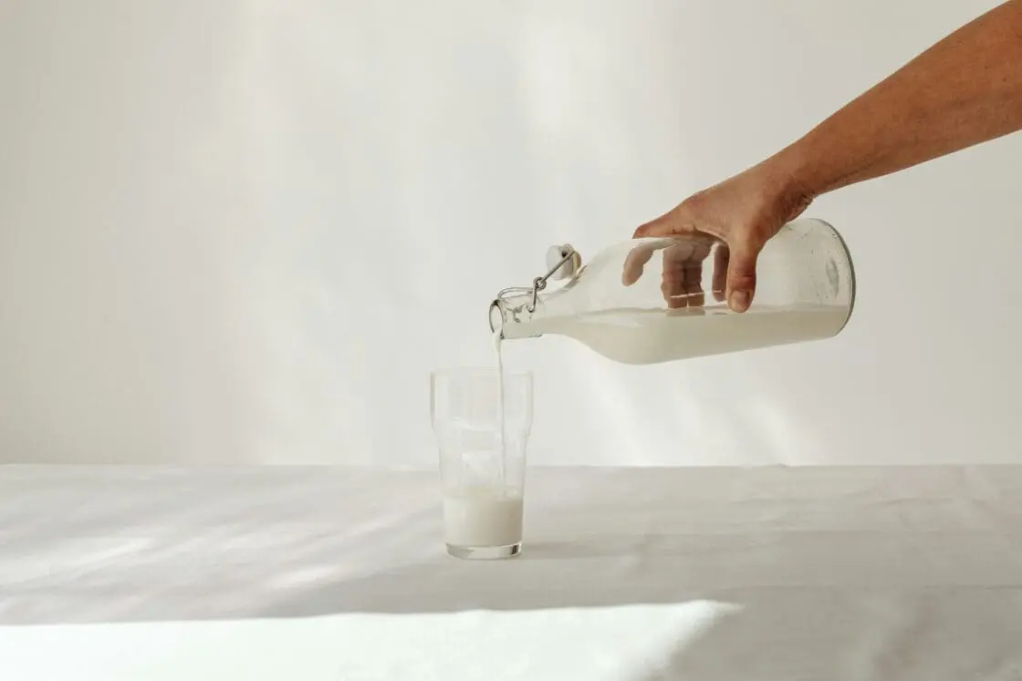Image of a female hand pouring dairy milk out of a glass container into a glass. The question is, is real dairy milk good for you?