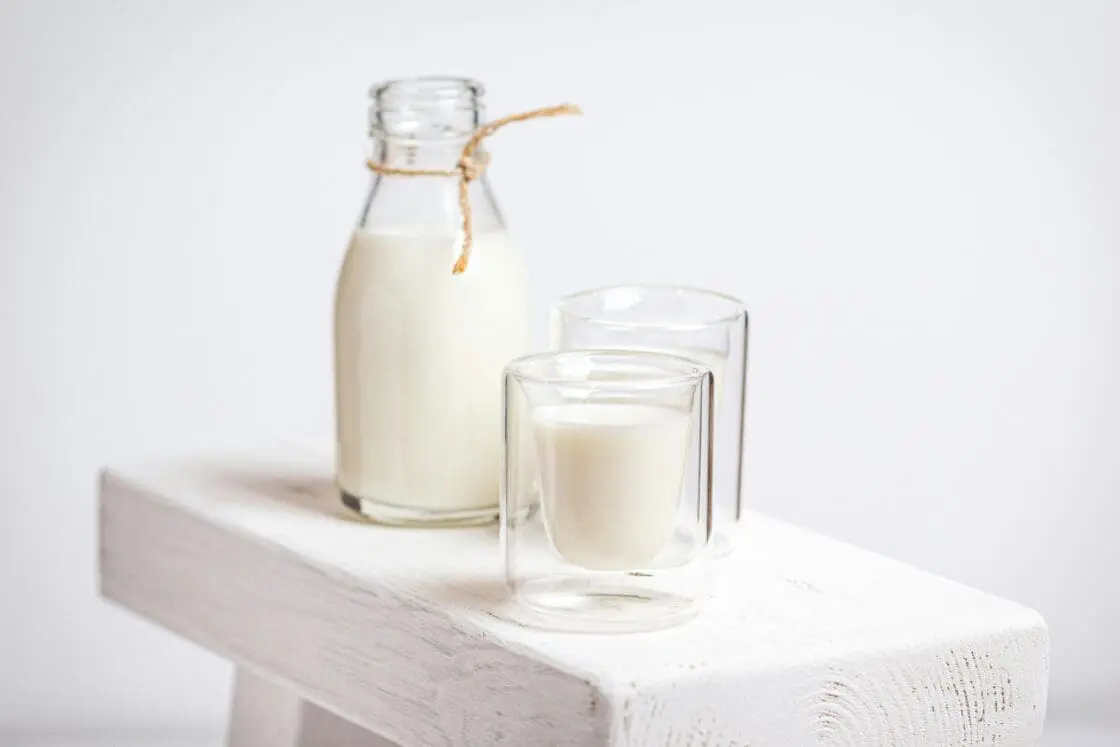 Image of two glasses of milk with a glass milk jug on a painted wood board. different types of milk have different health outcomes.