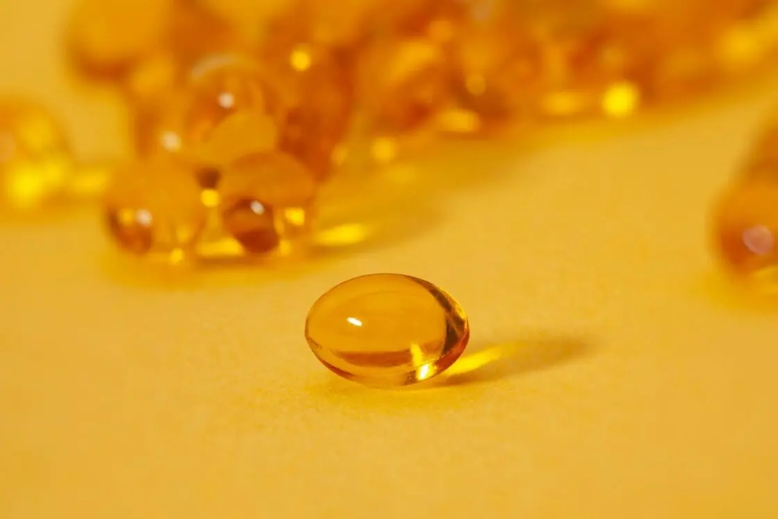 Image of a single cod liver oil or fish oil supplement, showcased on an orange background with many other supplements behind it.