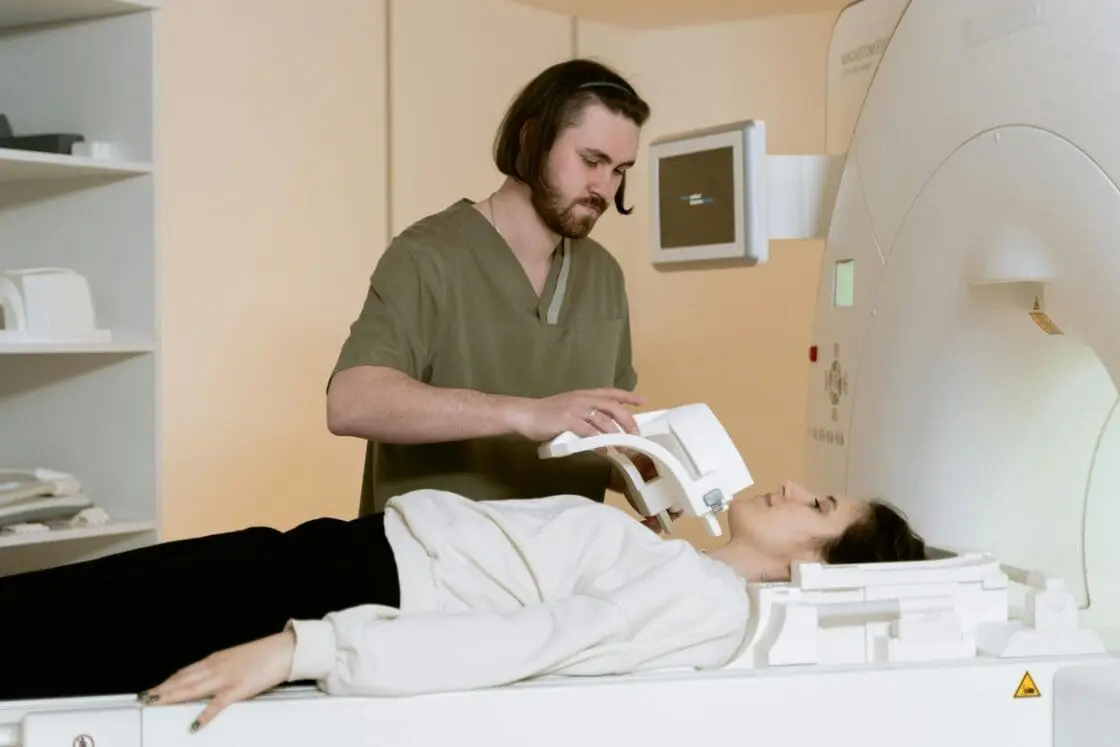 Image of a woman lying down in preparation for a full body scan, with a medical worker standing above her and getting ready to operate the machine.