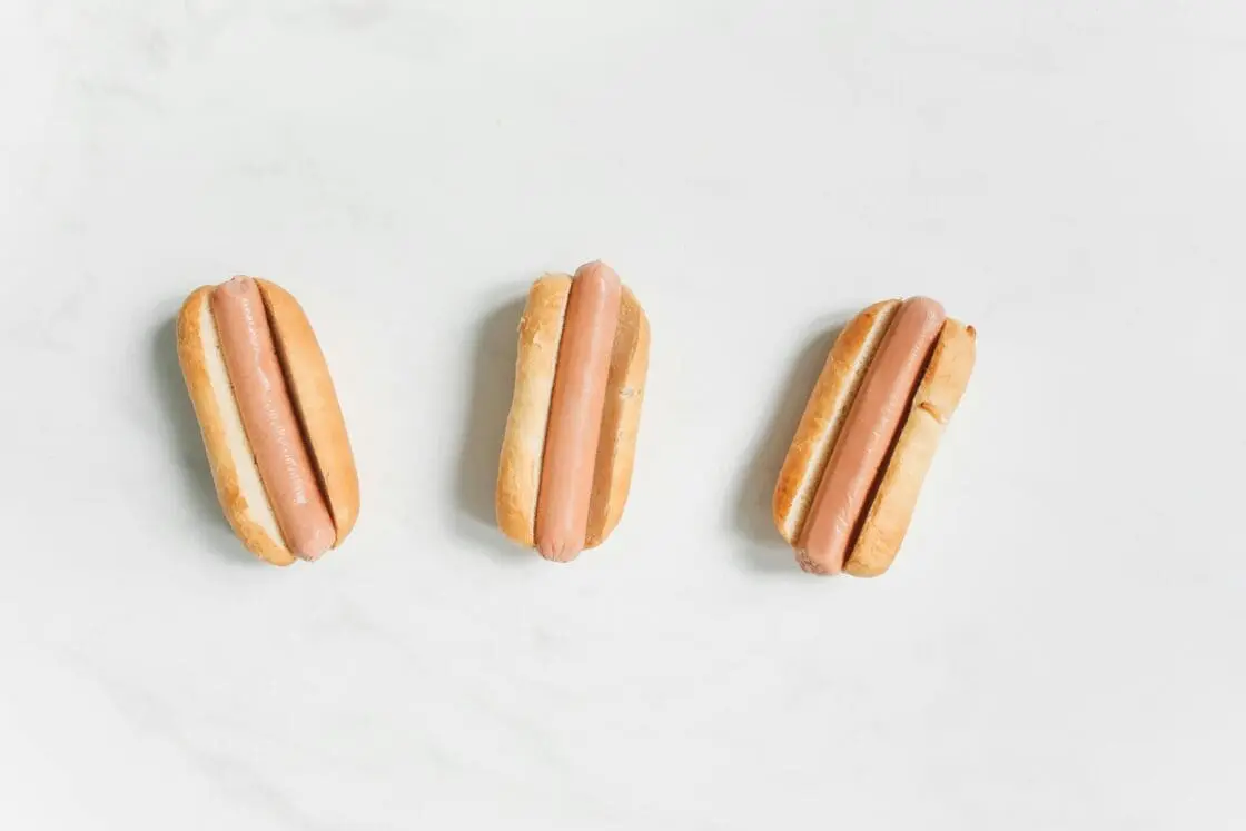 Image of three hot dogs in buns displayed against a white background.
