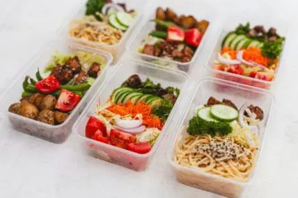 Image of six plastic food storage containers filled with prepped meals of noodles, vegetables, and proteins.