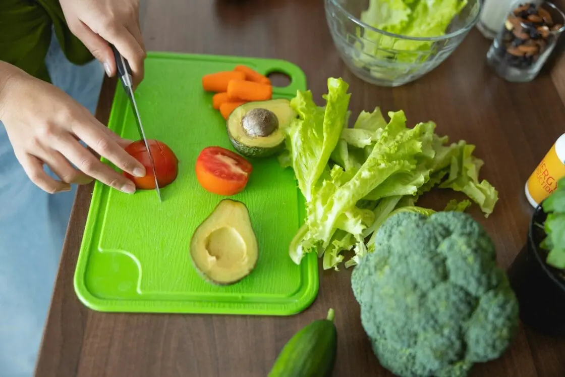 Image of hands slicing vegetables on a green plastic cutting board.