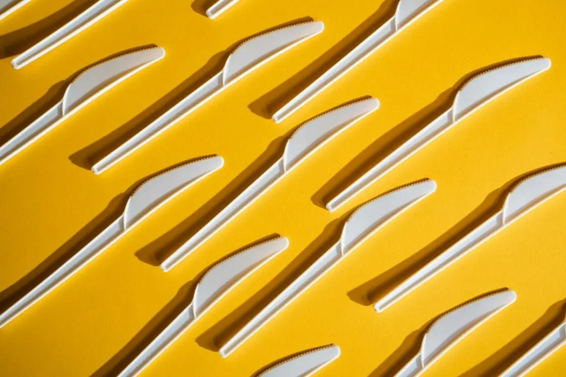 Image of white plastic knives in rows on a yellow background.