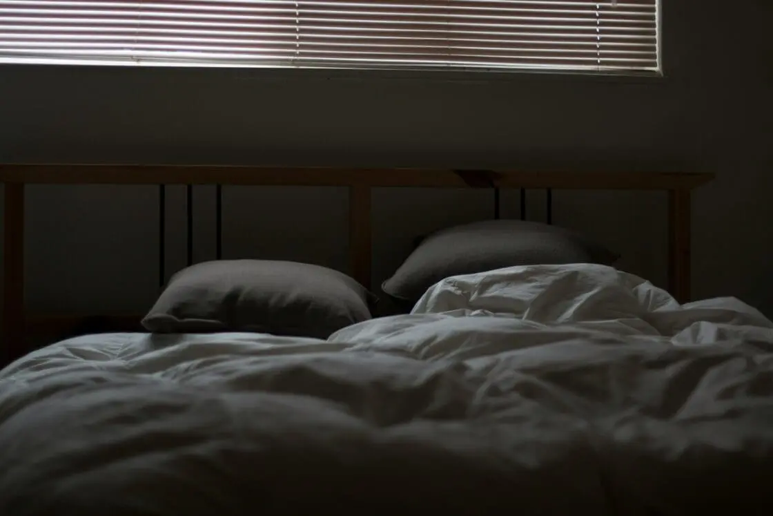 Image of a darkened bedroom with very little light illuminating a comfortable bed.