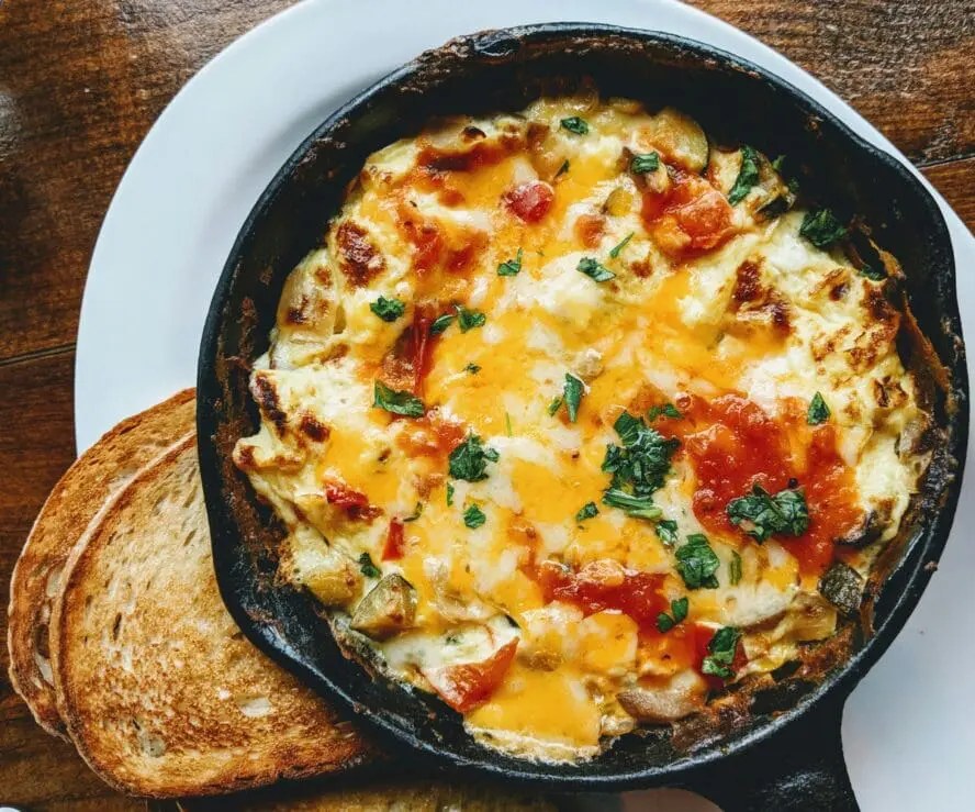 Image of a black cast iron pan with a cheesy egg and tomato mixture and a couple slices of sourdough toast.