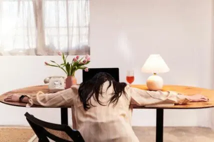 Image of a woman with her arms splayed on a desk in front of her laptop, with her head resting on the table.