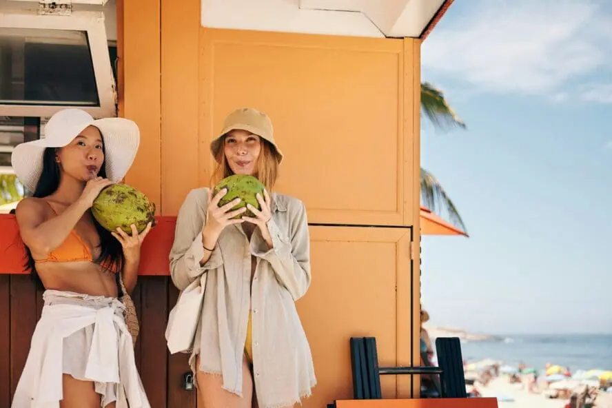 Image of two young women drinking fresh coconut water at the beach.