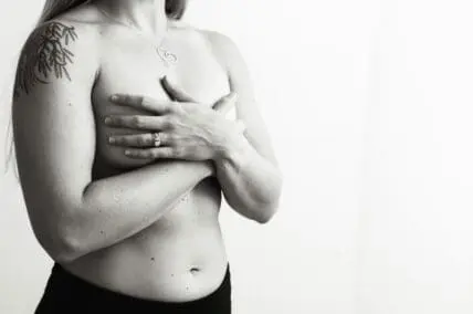 Black and white image of a woman's topless torso, with her hands crossed over her chest.