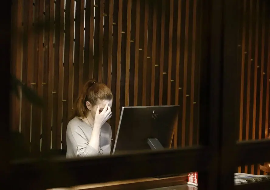 Image of a woman sitting with her face in her hand in front of a desktop computer.