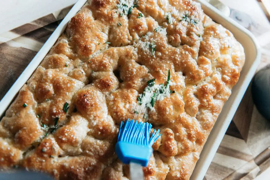 Image of herby garlic butter being spread onto a fresh pan of focaccia.