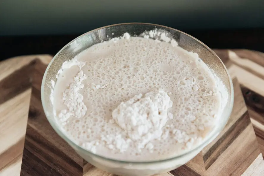 Image of a large glass bowl filled with yeast, warm water, and honey whisked to a foamy consistency for this focaccia recipe.