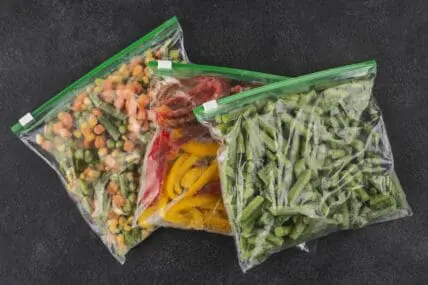 Image of three Ziploc bags filled with frozen vegetables set on a black marble counter.