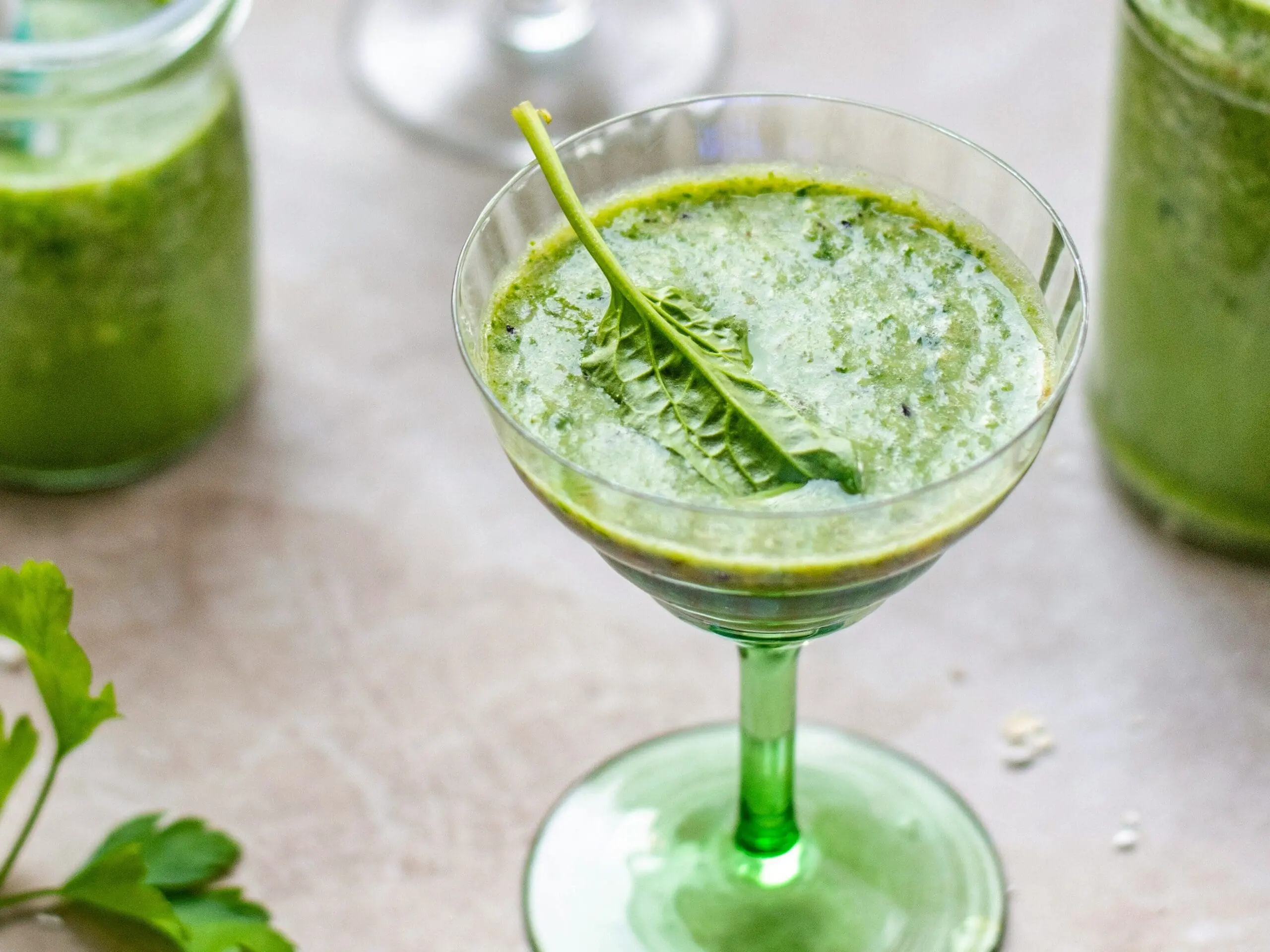 Image of a green juice drink in a coupe glass garnished with a single spinach leaf.