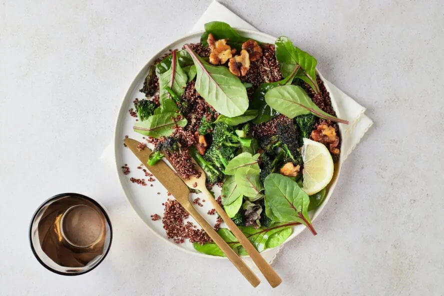 Image of a plate of leafy greens in an appetizing salad featuring spinach, quinoa, broccoli, and walnuts — several of the best foods for brain health.