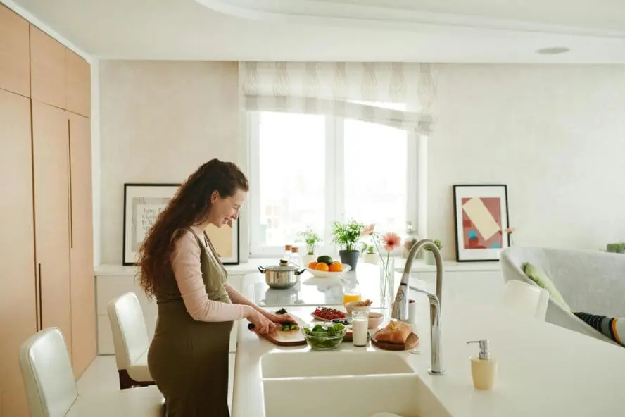 Image of a young pregnant woman standing at a counter in a bright kitchen, slicing some fruit.