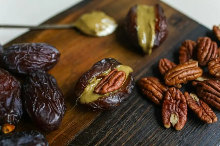 Image of several dates on a wooden board sliced open and stuffed with nut butter and walnuts.