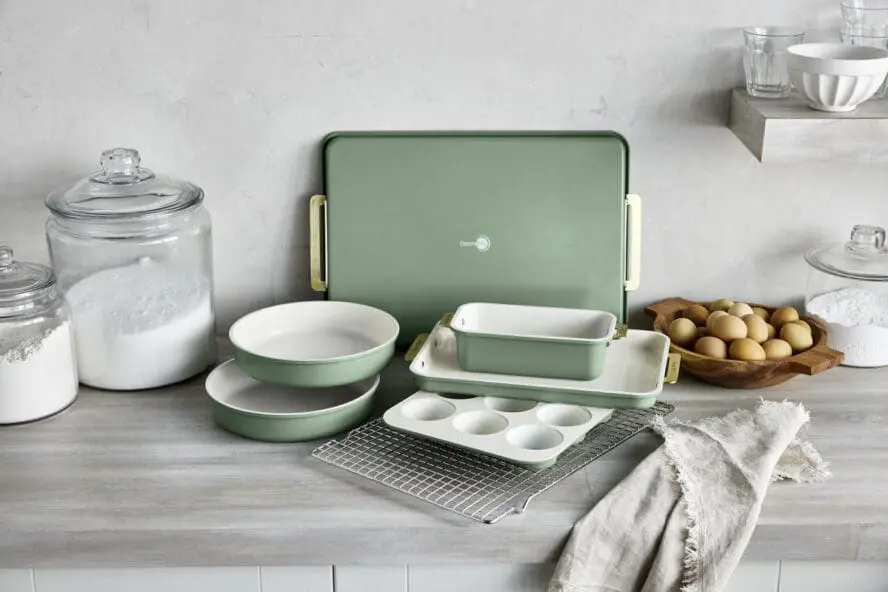 Image of the GreenPan Reserve Bakeware set (7 pieces) in sage green, displayed on a kitchen counter alongside eggs and flour.