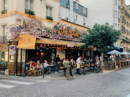 Image of a Parisian restaurant on a corner with outdoor seating and vines climbing up the walls.