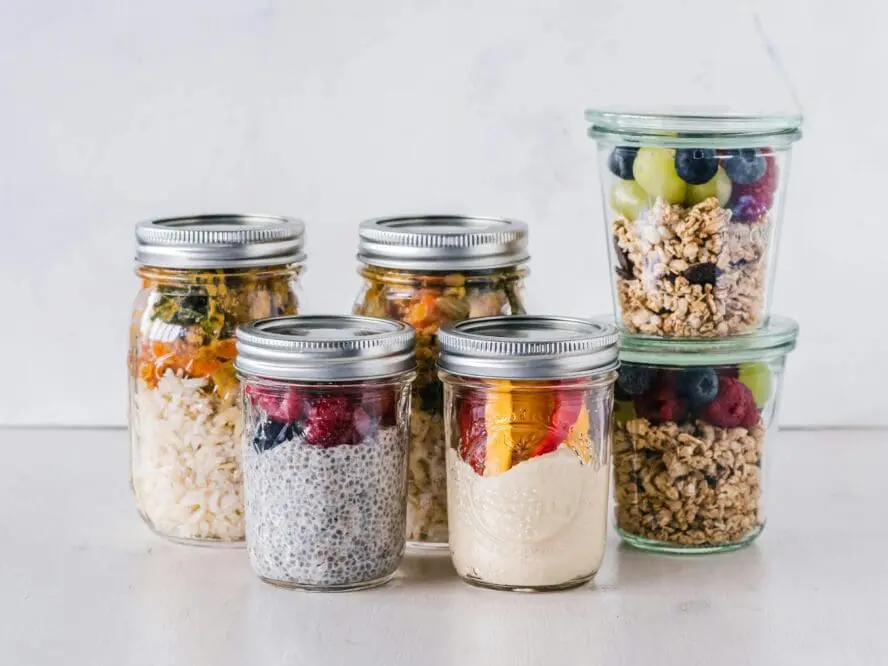 Image of glass mason jars filled up with various mixes of granola, chia seed puddings, fruits, and grain bowls.