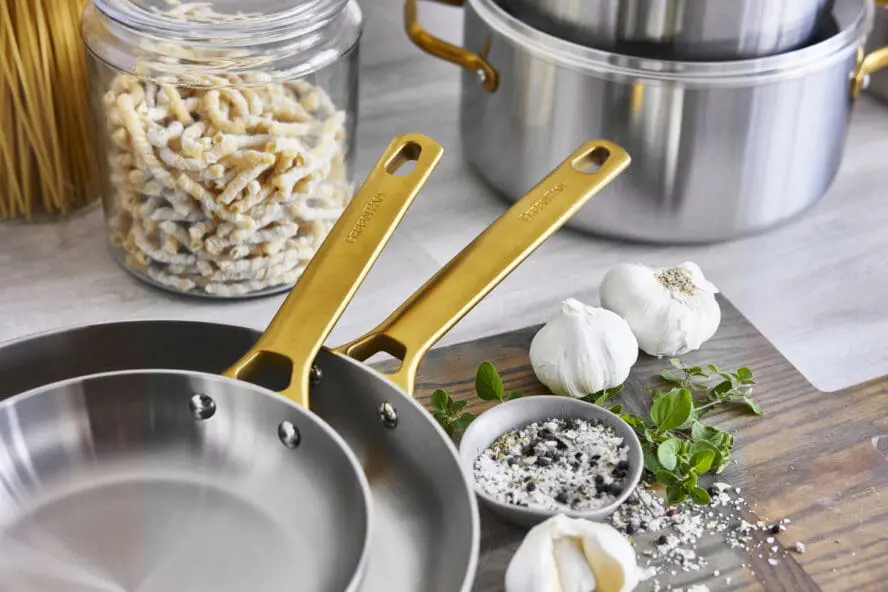 Image of two GreenPan Reserve Stainless Steel frypans nested in each other, with their iconic gold handles on display over a cutting board with garlic and truffle salt. 