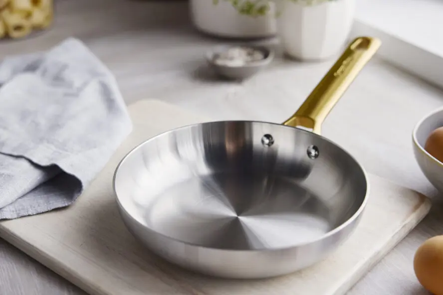 Image of a GreenPan Reserve Stainless Steel frypan displayed on a wooden cutting board in a brightly lit kitchen.