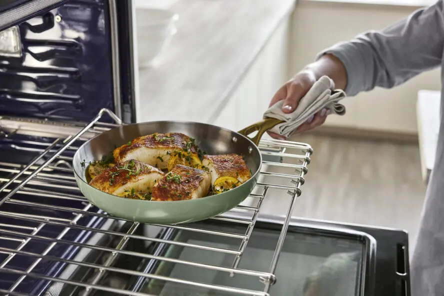 Image of a hand pulling a GreenPan Reserve Pro Stainless Steel frypan full of fish fillets out of the oven.