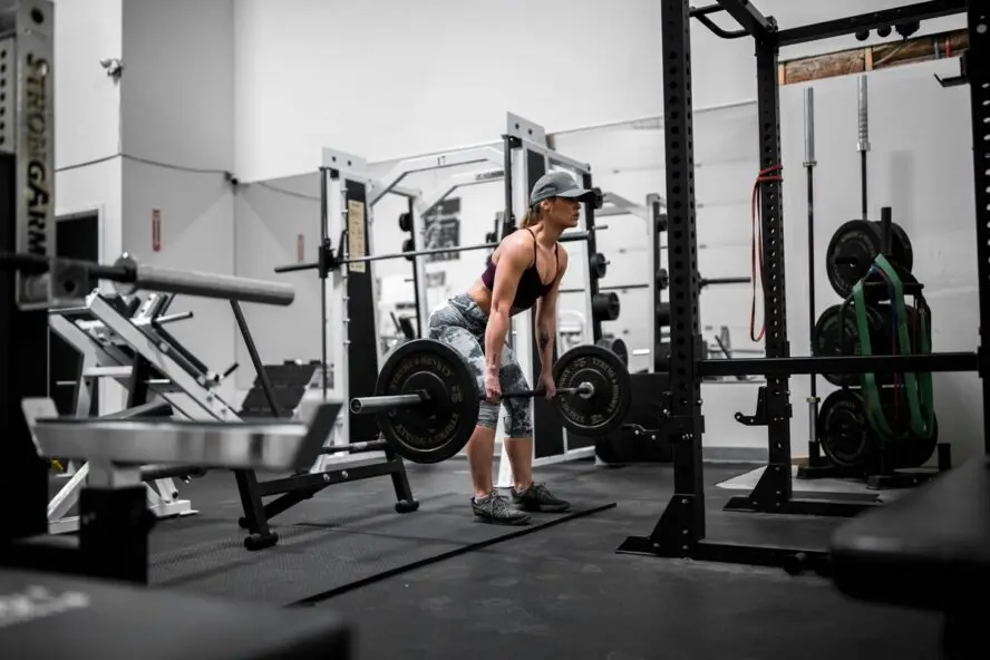 Image of a woman wearing a baseball cap and lifting a large barbell in an empty gym.