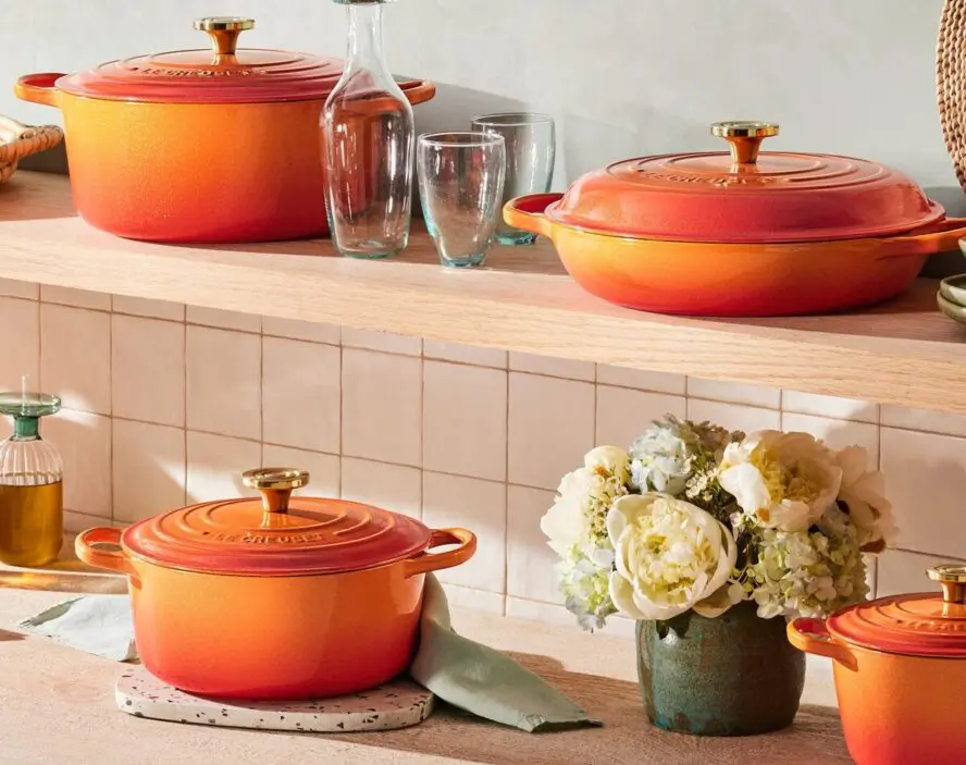 Image of several Le Creuset pieces displayed on a shelf in a beautiful kitchen, including an enameled Dutch oven.