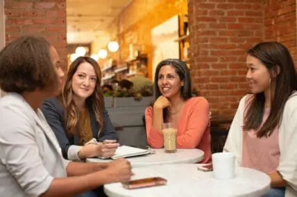 Image of four women sitting around a table at a cafe and chatting.