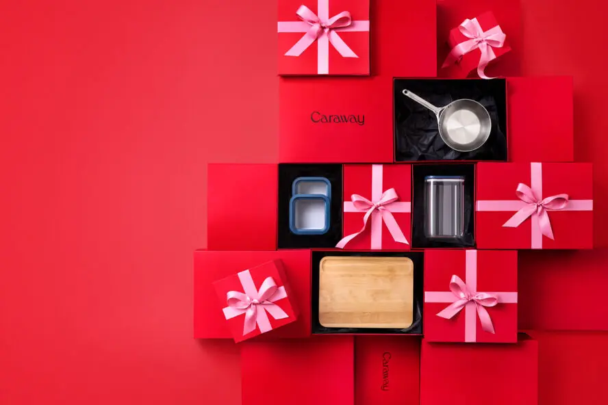 Image of several Caraway gift boxes with kitchen products wrapped up with pink bows on a red background.