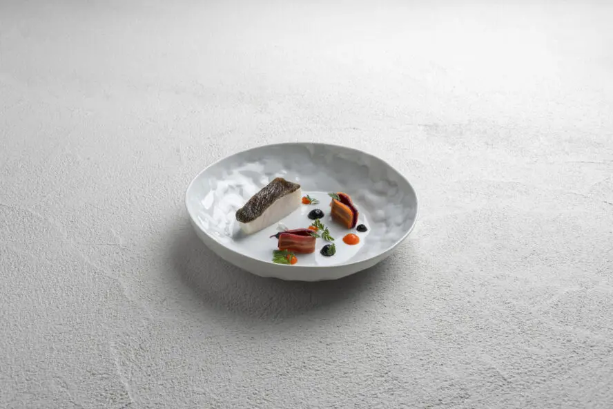 Image of a small plate with a beautifully arranged fish fine dining dish on it.