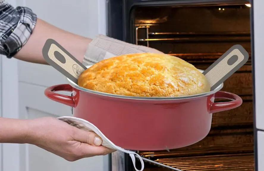 Image of a sourdough bread sling in a Dutch oven shown underneath a large loaf of sourdough bread.