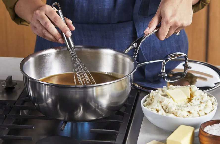 Image of the Demeyere Atlantis Saucier on a stovetop with someone whisking a brown sauce.
